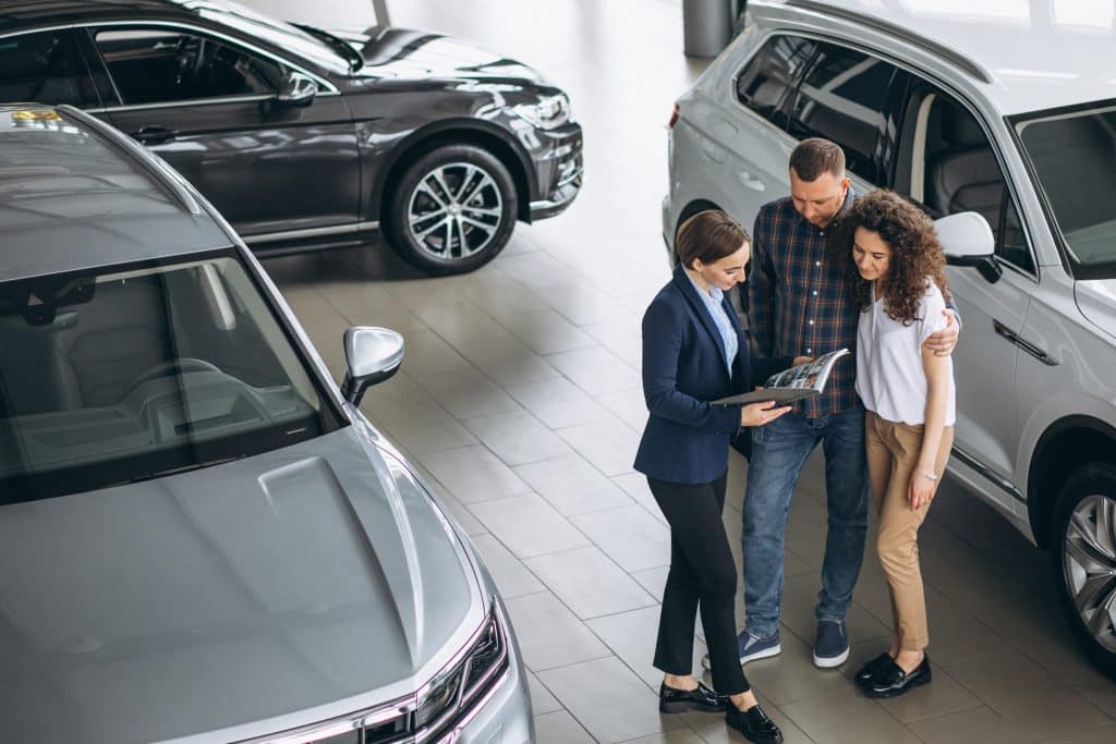 young couple talking sales person car showroom